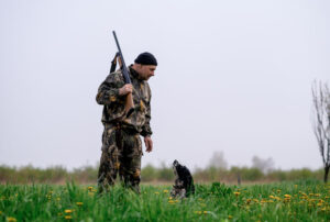 Male hunter with a gun on his shoulder stands with a dog while quail hunting