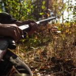 A hunter with a gun in his hands in hunting clothes in the autumn woods