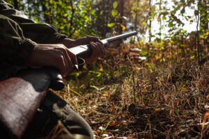 A hunter with a gun in his hands in hunting clothes in the autumn woods